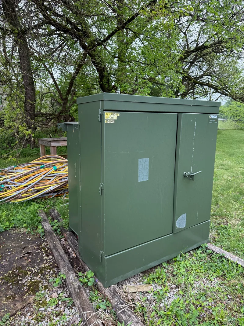 A green padmount transformer standing on a pad in grass